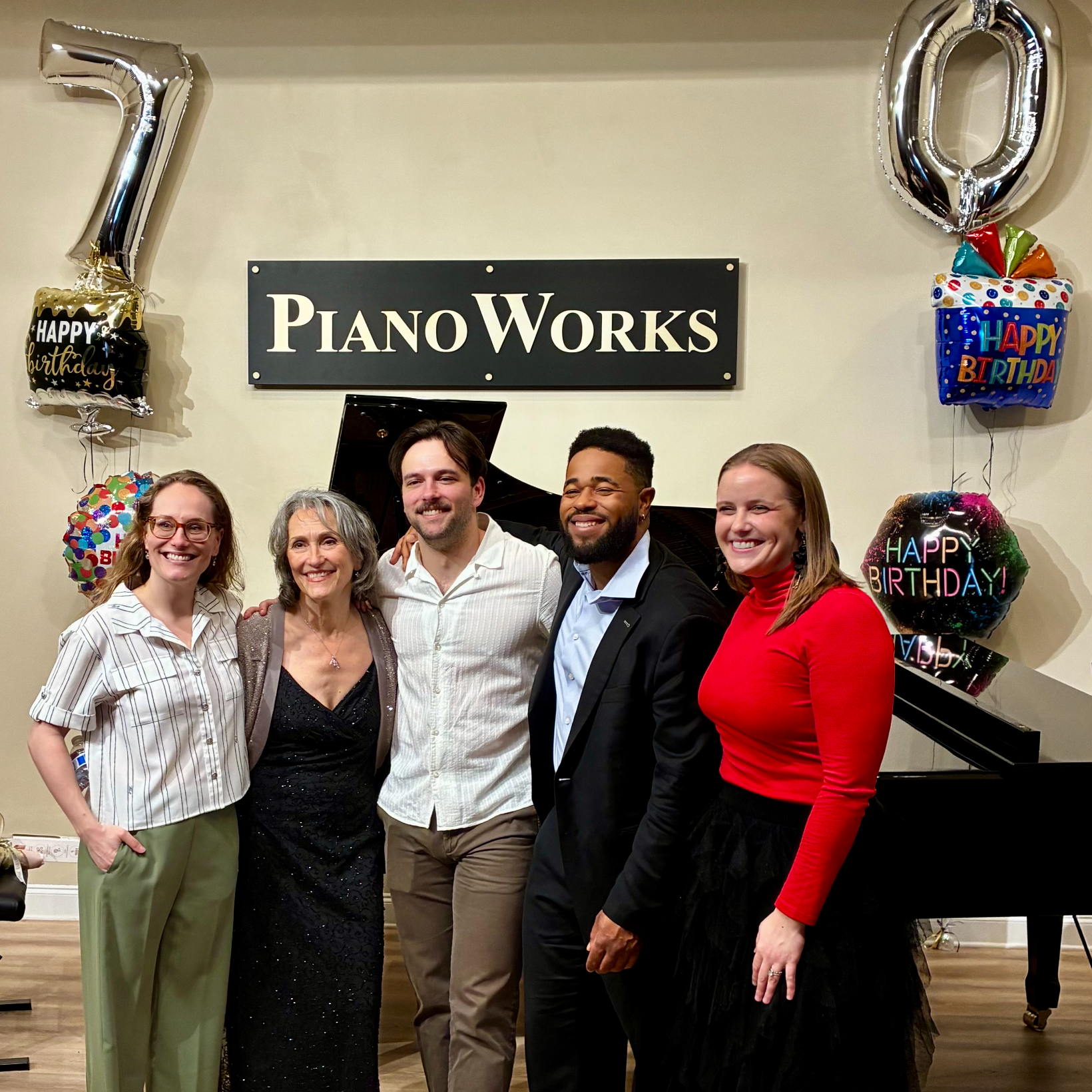 group of five smiling musicians standing in front of a piano