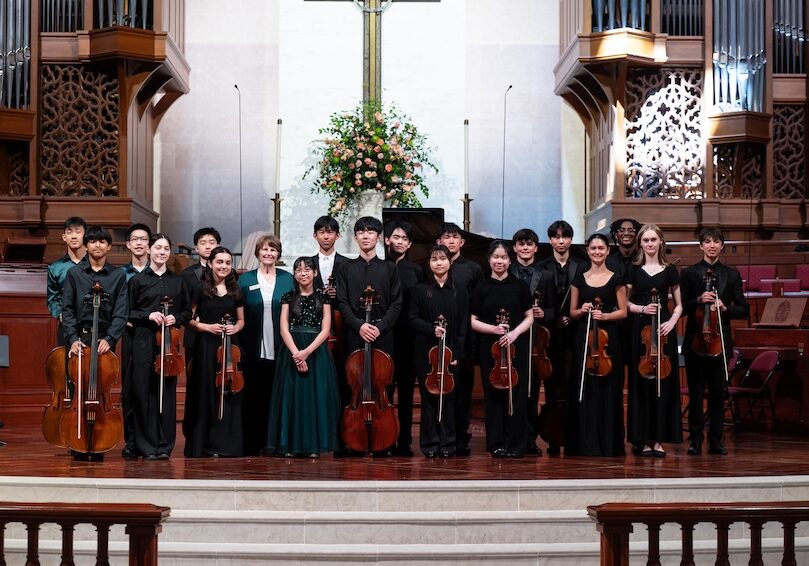 group photo of student musicians standing on stage with their instruments